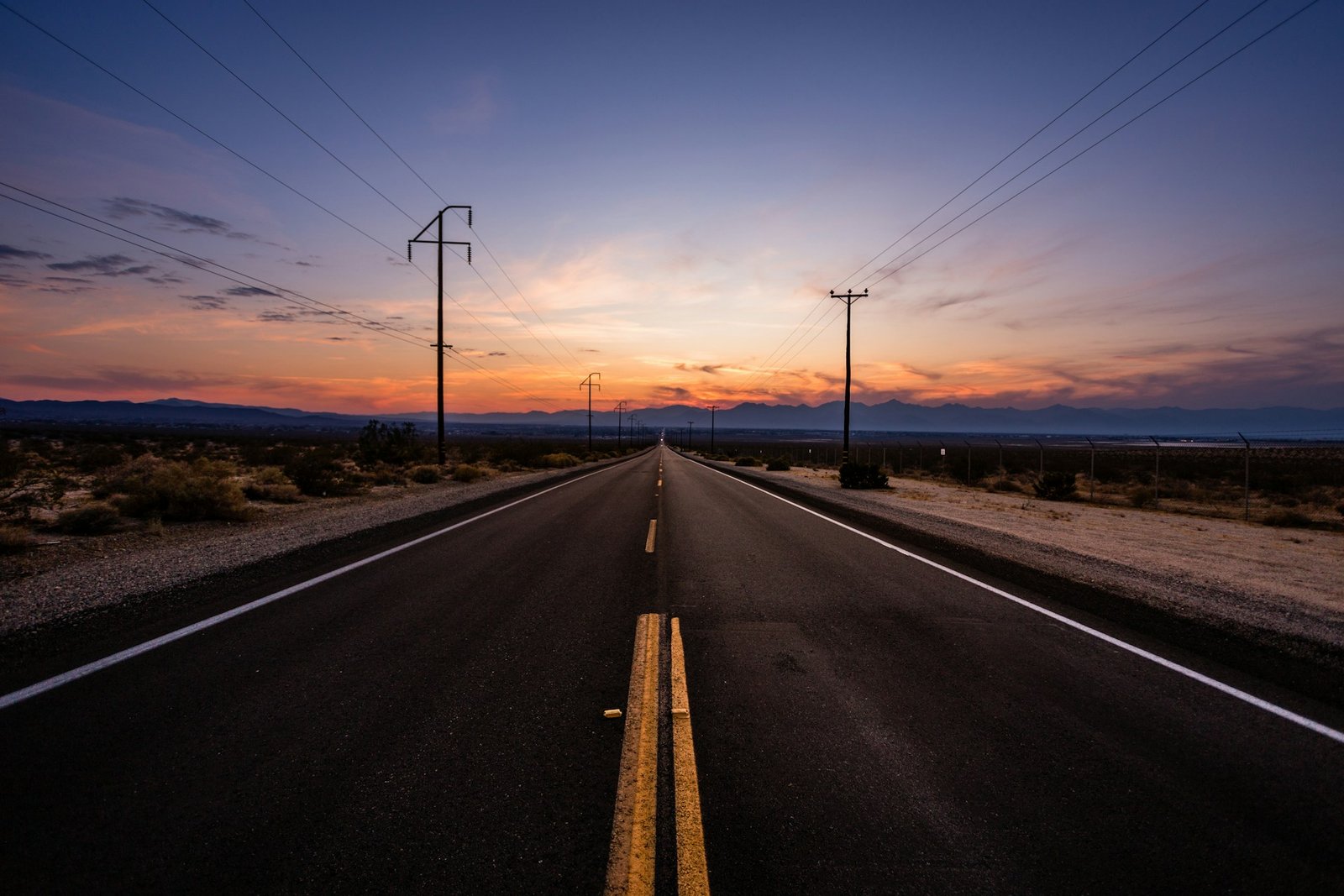 A straight desert road stretching to the horizon at sunset
