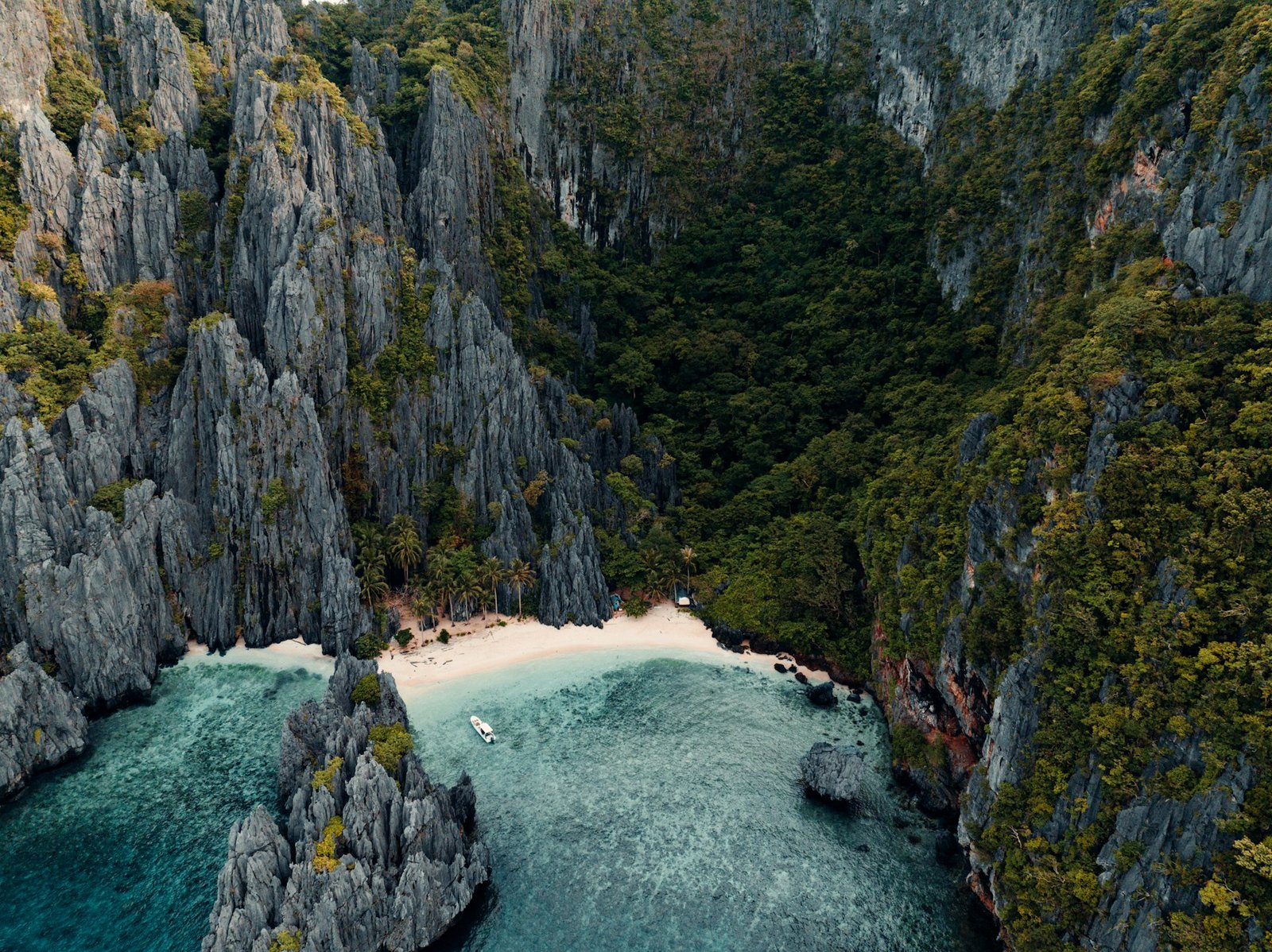 An aerial view of a hidden lagoon and white sand beach ringed by limestone cliffs and jungle